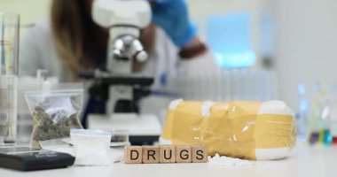 Kimya laboratuarındaki çeşitli narkotikler arasında tahta bloklardaki uyuşturucu metinleri. Kadın bilim adamı adli tıp laboratuarında mikroskop testleri yapıyor.