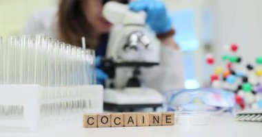 Teknisyen mikroskop kullanarak Kokain madde araştırması yapıyor. Test tüpleri ve moleküler modelle bilimsel ortamda analiz