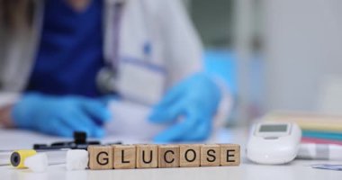 Doktor, klinikteki masasında glukometre ve tahta küplere glikoz yazarken tıbbi rapor yazıyor. Diyabet yönetimi ve yavaş bakım