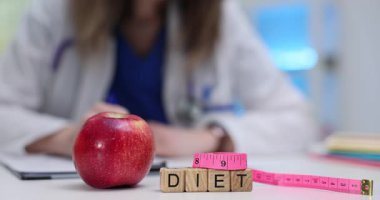 Kadın doktor, kırmızı elmanın yakınındaki hasta için diyet tasarısı hazırlıyor ve doktor ofisindeki masada bant ölçüyor. Modern klinikte sağlık ve beslenme