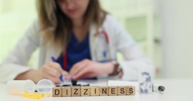 Kadın doktor masadaki haplar ve kapsüller arasında baş dönmesinin tedavisi için reçete yazıyor. Etkili ilaç kullanımı ve hasta bakımının önemi