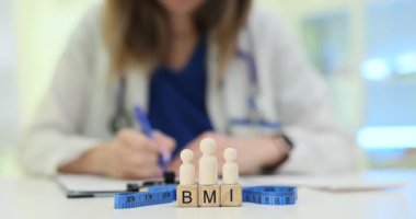 Kadın profesyonel BMI 'yi ağırlık yönetimi zorluklarını gösteren tahta heykelciklerin yanında değerlendiriyor. Hastanede sağlık değerlendirmesi ve obezite endişeleri