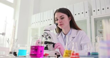 Kadın bilim adamı mikroskobu canlı kimyasal örnekleri incelemek için ayarlıyor. Araştırmacı tutarlılıktaki değişiklikleri tanımlamak için örnekleri karşılaştırır