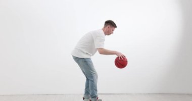 Sporcu, spor salonunun beyaz zemininde ritmik olarak basketbol topu sürüyor. Basit tişörtlü bir adam zıplama topu çevikliğini test etmek için elini kullanır. Yavaş çekim