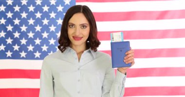 Kendine güvenen bir iş kadını, pasaportunda vize ve uçuş kartıyla Amerikan bayrağına karşı onay veriyor. Mutlu bayan uluslararası seyahate hazır.