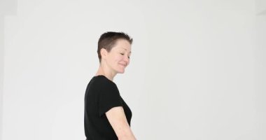 Kısa saçlı kadın beyaz arka planda yürürken davetkar bir jest yapıyor. Dost canlısı kadın, el sallayan dikiz görüntüsünü takip etmek için ağırdan alıyor.