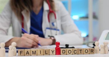 Aile Doktoru ahşap bloklarda masanın üzerinde rakamlarla ifade et. Kadın hekim, hastane işyerinde oturan hasta tıbbi kayıtlarıyla çalışıyor.