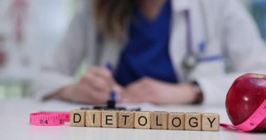 Kadın doktor beslenme uzmanı, dietoloji harfli tahta küplerin yanında diyet planı yazıyor. Ölçüm bandıyla kırmızı elma sağlıklı yaşam tarzını gösteriyor