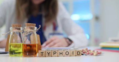 Kadın doktor masada üzerinde tifo, sarı ve turuncu sıvı yazan reçeteler yazıyor. Klinikte bulaşıcı hastalık tedavisine odaklanın