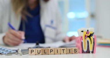 Kadın doktor Pulpitis tedavisi için tıbbi ofiste reçete yazıyor. Masanın üzerine belirgin bir şekilde yerleştirilmiş posanın iltihaplanmasını gösteren diş modeli.