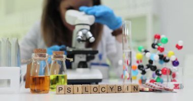 Bilim adamı laboratuarda test tüpleri ve moleküler modelle Psilosibin 'i analiz eden mikroskop kullanıyor. Potansiyel tıbbi uygulamalar ve kimyasal özellikler