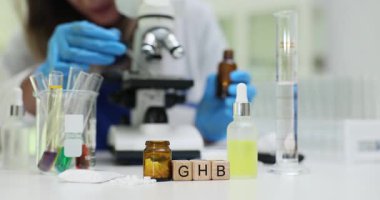 Koruyucu eldivenler giyen bilim araştırmacısı yüksek güçlü mikroskop altında GHB örneğini inceliyor. Laboratuvarda gama hidroksibürik asit araştırması.