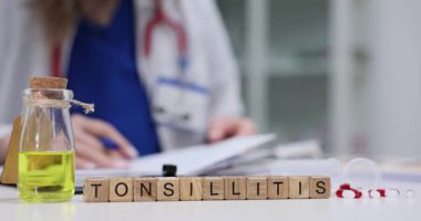 Tıbbi pratisyen, masasında ilaç şişesi ve ilaç şişesi ile bademcik iltihabı teşhisi koyan belgeleri özenle hazırlar. Klinik ortamında hasta bakımı