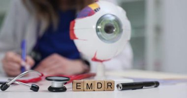 Doktor, tahtadan küplerin yanında EMDR ve masasında anatomik göz modeli olan kağıtları inceliyor. Tıbbi çalışma alanında psikolojik travma terapi teknikleri.