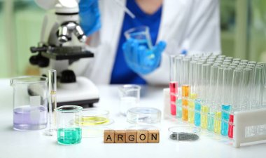 Kendini işine adamış bir bilim adamı renkli laboratuvar çözümleri ve temel laboratuvar araçlarıyla çevrili bir mikroskop kullanır.