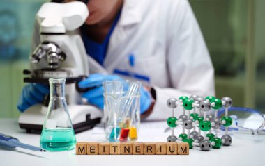 Bir araştırmacı, çeşitli laboratuvar ekipmanlarıyla birlikte güçlü bir mikroskop kullanarak birden fazla deney yürütür.