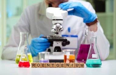 Bir bilim adamı mikroskop, renkli test tüpleri ve gelişmiş aletlerle örnekleri inceliyor.