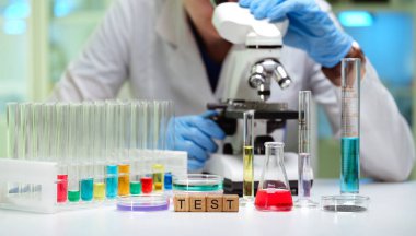 Çalışkan bir araştırmacı, devam eden deneyler için test tüpleriyle çevrili örnekleri mikroskop altında inceler.
