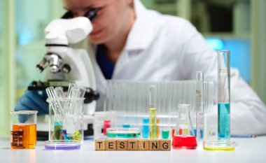 Bir araştırmacı, bilimsel testler için test tüpleri ve reaktörlerle çevrili mikroskop kullanarak örnekleri inceler..
