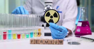 Etrafında renkli test tüpleri ve nükleer sembollerle Fermium 'un incelendiği canlı bir laboratuvar sahnesi.