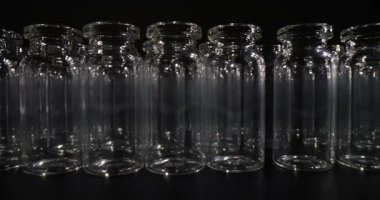 Cam şişeler, şeffaf siluetlerle geometrik desen oluşturan kompakt hizada dururlar. Derin gölgeli arkaplan minimalist tasarımı vurguluyor