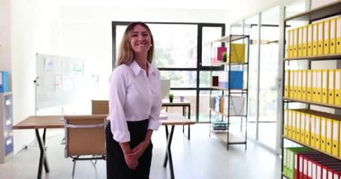 Profesyonel iş kadını, raflarında renkli yüzük klasörleriyle ofise gelen ziyaretçiyi kendinden emin bir şekilde karşılıyor. Çağdaş kurumsal ortam