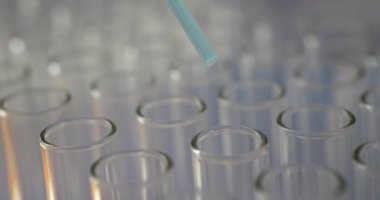 Pipette mavi sıvıyı tek saydam test tüplerine damlatıyor. Temiz test tüpleri rengin tam görünürlüğünü ve sıvının tutarlılığını sağlar. Yavaş çekim