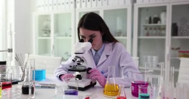 Araştırmacı bilimsel örneği mikroskop merceğiyle inceliyor. Kadın, netlik için mikroskop düğmesini ayarlamaya odaklanıyor.