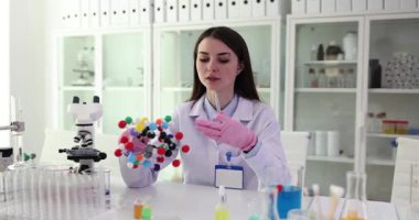 Kadın bilim adamı moleküler yapıyı molekül modeli üzerinde inceliyor. Esmer araştırmacı, odak düğmesini tam olarak ayarlamak için mikroskop altında örnek gözlemler.