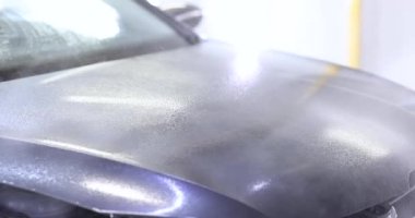 İşçi seramik kaplamayı araba kaputunun yüzeyine eşit olarak uyguluyor. Deneyimli teknisyen sprey kullanarak ürünü hassasiyetle uygular. Yavaş çekim