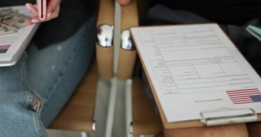İş adamları, konsolosluktaki toplantı sırasında etrafları Amerikan bayrakları ve paralarıyla çevrili vize formlarını dolduruyorlar. Seyahat ve göç konuları