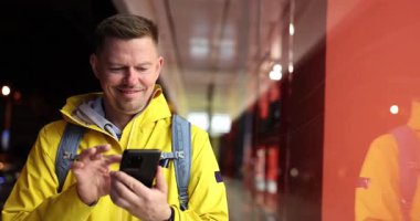 Sırt çantalı parlak sarı yağmurluk giyen mutlu turist gece akıllı telefon kullanıyor. İnsan, takipçilerle bağlı kalarak kentsel keşiften zevk alır.