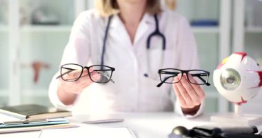 Kadın göz doktoru, gözlüklerinin anatomik göz modeliyle el ele oturduğunu gösteriyor. Görüş düzeltmesi için çerçeve seçimi teklif et