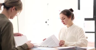 İş kadınları modern ofis masasında oturup belgelerini gözden geçirir ve proje üzerinde işbirliği yaparlar. Etkili takım çalışması ve ofiste odaklanmış iletişim