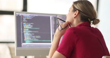 Kadın yazılım geliştirici yeni uygulama programı üzerinde çalışıyor. Gözlükleri elinde tutuyor ve dikkatlice monitöre bakıyor. Programlama sorununu çözmeye odaklan