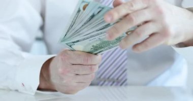 Beyaz gömlekli ve kravatlı bir erkek ofis çalışanı ofiste yüklü miktarda 100 dolarlık banknot sayıyor. Finansal başarı ve kurumsal zenginlik birikimi