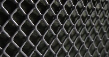 Metalik çit örgüsü tekrar eden elmas desenleri yaratır ve dokulu arka plan oluşturur. Işık ve gölge koyu tasarıma derinlik ve kontrastı ekler