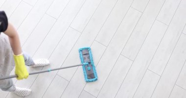 Sarı eldiven giyen hizmetçi titizlikle beyaz lamine zemini modern mavi paspasla temizliyor. Dairenin hijyen ve bakımının önemi