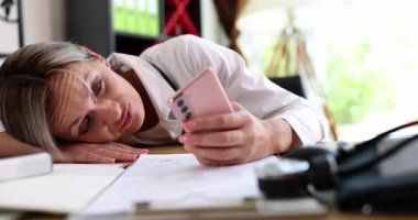 Çok çalışan ve yorgun bayan profesyonel akıllı telefon tutarken masa başında dinleniyor. Çağdaş hastane ortamında uzun ve stresli bir değişim