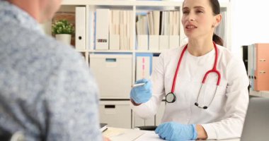 Eldivenli kadın doktor, erkek hasta konsültasyonu sırasında elinde kalem tutuyor. Klinik ortamda teşhis konuyor. Profesyonel sağlık hizmeti etkileşimi