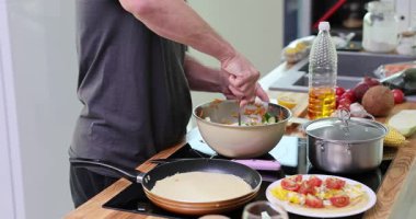 Adam tezgahta malzemelerle çevrili salatayı kasenin içinde karıştırıyor. Erkek dokuyu birleştirir ve aile ağır çekim için sağlıklı öğle yemeği hazırlamaya odaklanır.