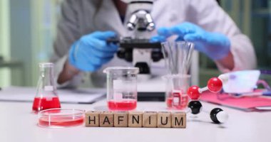 Yüksek teknolojili bir laboratuvar ortamında kendini adamış bir bilim adamı Hafniyum örneklerini mikroskopla inceliyor.