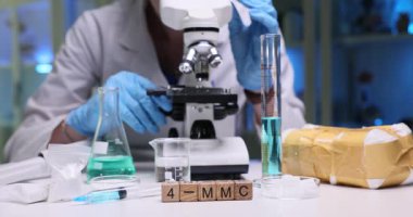 Bir bilim adamı laboratuvarda çalışıyor. Araştırma için çeşitli reaktörlerle mikroskop altında örnekler inceliyor.