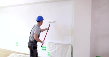 Miğferli adam boş odada duvarları fırçayla boyuyor. Tulum giyen işçiler ofisin yüzeyine beyaz renk yayarlar. Ev yapılandırması