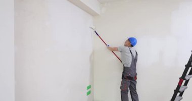 Üniformalı çalışanlar yeni evlerinde duvarları fırçayla boyuyor. İşçi, ofisteki düz yüzeye beyaz renk uygular. İç geliştirme