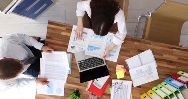 Masadaki çalışanlar, iş toplantısını gösteren çizelgeler ve grafiklerle belgeleri incelemeye odaklanmış durumdalar. Tablonun üzerindeki sabit çalışma aktif iş önerir