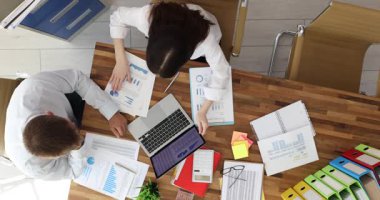 Meslektaşlar, ofisteki dizüstü bilgisayarlarla kaplı ahşap masada iş birliği yaparlar. Erkek ve kadın dizüstü bilgisayarı işaret ediyor diyagram tartışmasını öneriyorlar