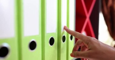 Kadın, açık yeşil klasörlerin omurgasını işaret ediyor. Organizasyonu işaret ediyor. Modern ofis arşiv ayarlarında özel belge seçme eylemi