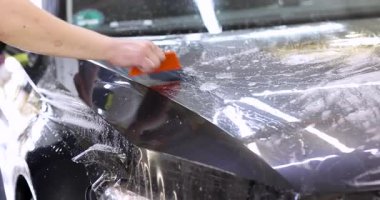 Erkek işçi yıkandıktan sonra arabadaki suyu turuncu cam sileceği ile temizler. Araç yüzeyinde seri olmayan bitirme işleminin bir parçası