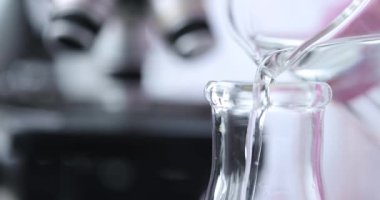 Kimyager şeffaf sıvıyı kavanozdan uzun cam kaplara döker. Işık suyun içinden geçer ve yüzeyde parlak gölgeler yaratır.